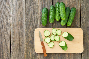 Whole and sliced ripe cucumbers on a cutting board, top view.