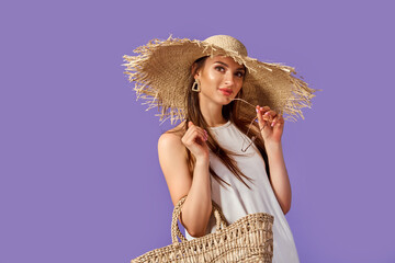 Beautiful young woman in white dress, summer straw hat, sunglasses, straw bag isolated on pastel violet background. 