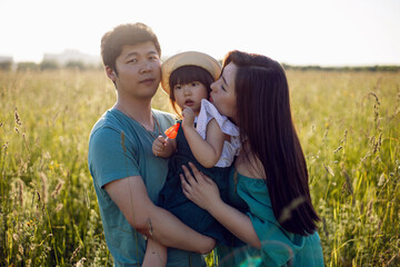 Korean family with their daughter go to the field in the grass at sunset