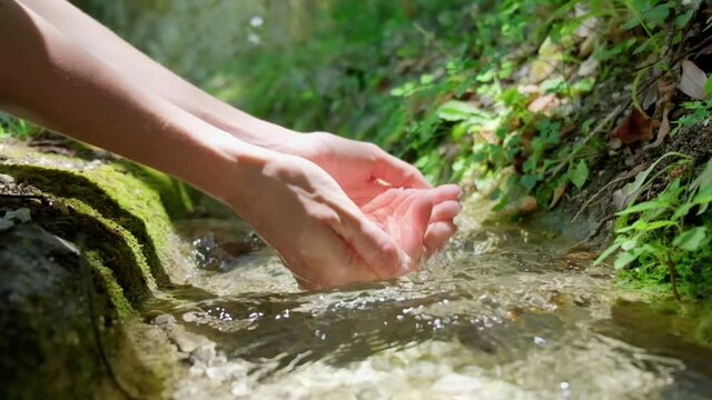 Female hand touching fresh spring water in forest creek, slow motion of pure stream water.