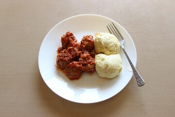 Meatballs in tomato sauce and puree dish on a white plate with a fork on wooden background. Top view, selective focus