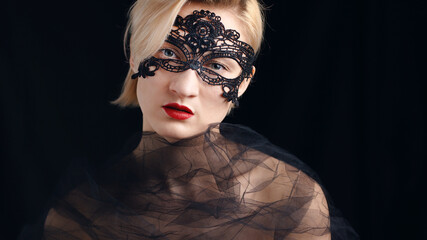 A blonde model dressed in a masquerade ball costume for the fancy costume party. Wearing A Venetian Masquerade Mask and red lipstick. Closeup headshot. Mysterious girl wearing a Masquerade mask.