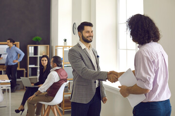 People exchanging a handshake confirming collaboration, greeting each other or thanking each other for help. Two happy businessmen or office colleagues shaking hands as they meet in a business meeting