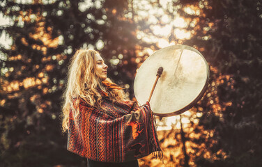 beautiful shamanic girl playing on shaman frame drum in the nature.