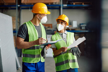 Warehouse workers cooperating while going through shipment list in storage room during COVID-19 pandemic.