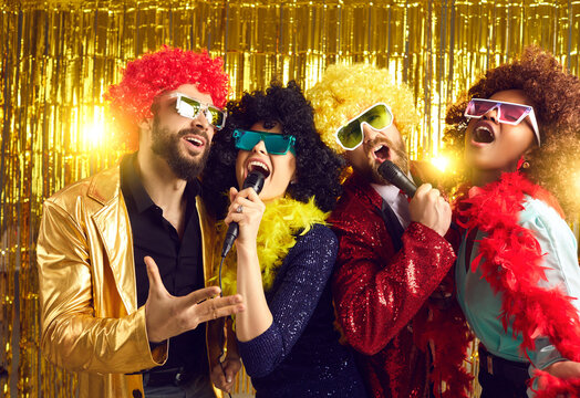 Karaoke friends party, birthday holiday event celebration in nightclub. Group of diverse team mates in funny wig and costume having fun dancing and singing together in microphone with pleasure