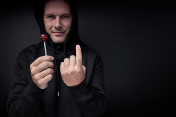 creepy threatening adult man in black wear offering candy lollipop to children standing on black...