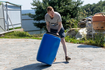 a man rolls a blue barrel at the dacha