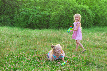 Naklejka na ściany i meble two little girls play in the summer on a green meadow with water pistols