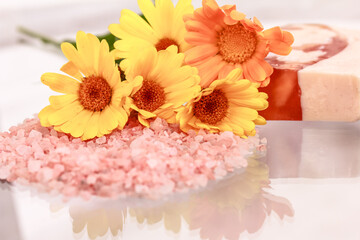 Calendula flowers, seal salt and natural orange-colored soap bar on glass table. Aromatherapy, spa and wellness concept