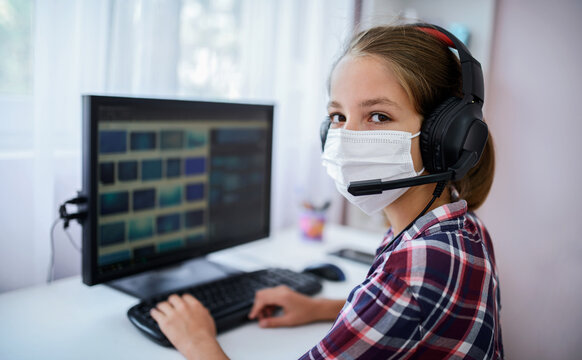 Little girl with protective mask on her face learning online lessons during detention at home. Education, medical concept