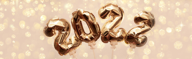 Golden numbers 2022 from New Year's balls of yellow metallic color on a background of bright bokeh from the lights. The concept of a happy and healthy new year and Christmas. Banner