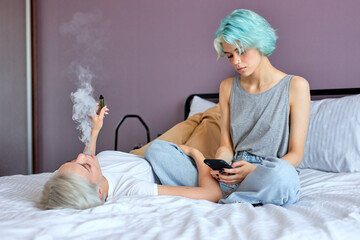 Two pretty best friends forever girlfriend talk, relaxing, smoking and surfing the Net while lying...