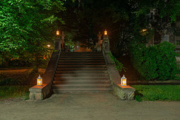 Park w mieście Iłowa w Polsce w nocnej scenerii. Ciemności rozświetlają lampiony ustawione na kamiennych schodach. - obrazy, fototapety, plakaty