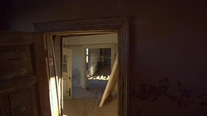 Abandoned building being taken over by encroaching sand, walking through doorways in the ghost town of Kolmanskop near Luderitz, Namib Desert, Namibia, Africa.