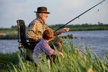 family, generation, summer holidays concept. caucasian grandfather and grandson with fishing rods...