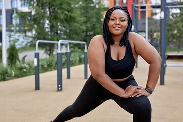 adorable fat woman in black tracksuit is engaged in fitness on sports ground, side view portrait....