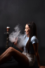 The girl smokes a hookah on a black background. Smoke comes out of the mouth. The pleasure of smoking
