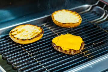 Cheese on cutlet grilling for cheeseburger. Grilling burger on mangal. Two burger buns and one cutlet are being cooked on a barbecue grill. Delicious homemade burger