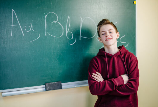 Successful schoolboy showing notes at the blackboard in school. Boy working in class and feeling smart. English lesson concept