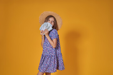 Portrait of little caucasian girl with long hair in summer dress holds a lot of money isolated on yellow background