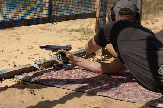 Man in tactical clothes shooting from a pistol, reloading the gun and aiming at the target in the open-door Shooting range