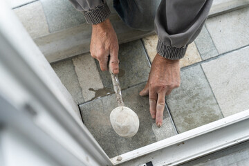 Close up on hands of unknown senior man craftsman using hammer to adjust and lay ceramic tiles on the balcony or terrace over adhesive cement in day - construction industry concept copy space