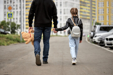 Pedophile man holds the hand of teenage girl in street. The concept of kidnapping and child trafficking. Rear view on pedophile with toy and caucasian child girl walking along the street. Crime - obrazy, fototapety, plakaty