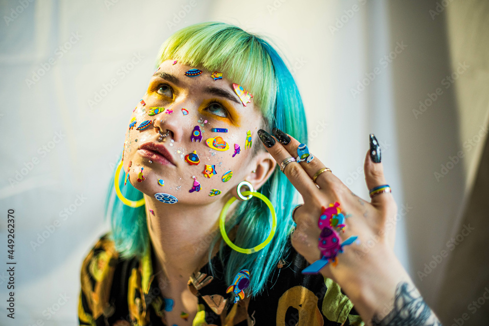 Wall mural Closeup fashion portrait young pretty beautiful girl with green and blue hair. Beautiful fashion girl with luxury professional makeup and funny emoji stickers glued on the face. Young woman