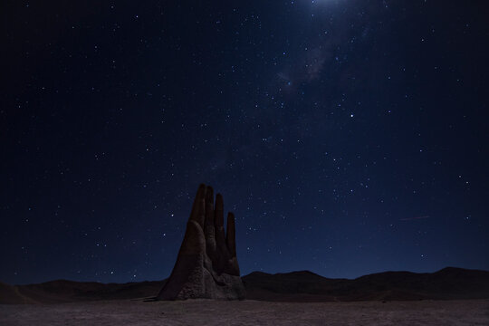 Hand of the desert in Antofagasta, Chile. Night long exposure shot with sky full of stars. Moonlight and a shooting star can be seen.
