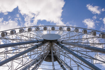 Large white Ferris wheel against the blue bright sky, bottom view. Concept entertainment.
