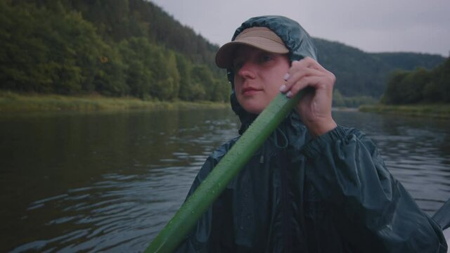 Rafting at rain. Young woman sits on the raft in raincoat and paddles during the rainy day