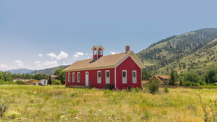 Old red school house at Maysville, Colorado surrounded with grass.