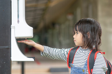 Child girls kid using automatic alcohol gel dispenser spraying on hands sanitizer machine antiseptic disinfectant, new normal life after Coronavirus COVID-19 pandemia.