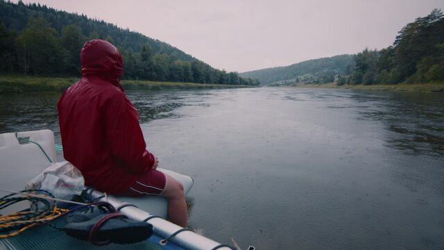 Rafting at rain. Young man sits on the raft in raincoat and paddles during the rainy day