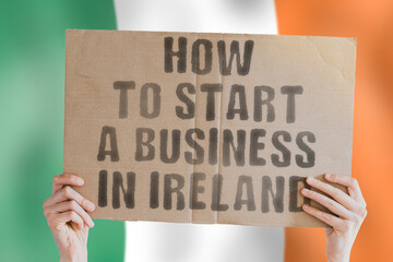 The phrase " How to start a business in Ireland " on a banner in men's hand with blurred Irish flag on the background. Business. Money. Company. Law. Illegal. Lawyer. Earnings. Job.