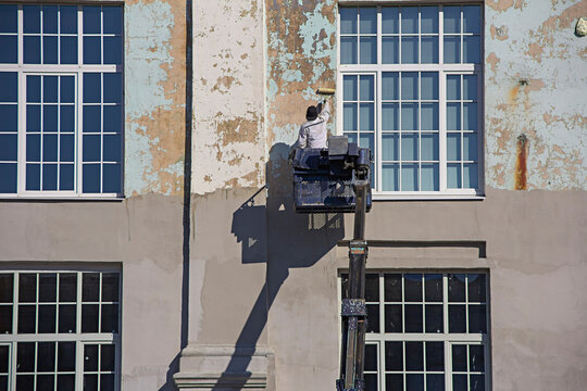 Commercial painter at the mobile crane truck cradle painting a building wall that being repaired