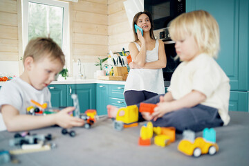 Happy family a young mother is talking on the phone and the children are a small beautiful baby son. They play a children's construction kit with different colored parts.