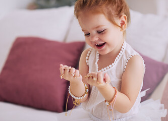 cute baby girl feeling happy trying on a lot of finger rings and bracelets, bijou jewelry - 449273732