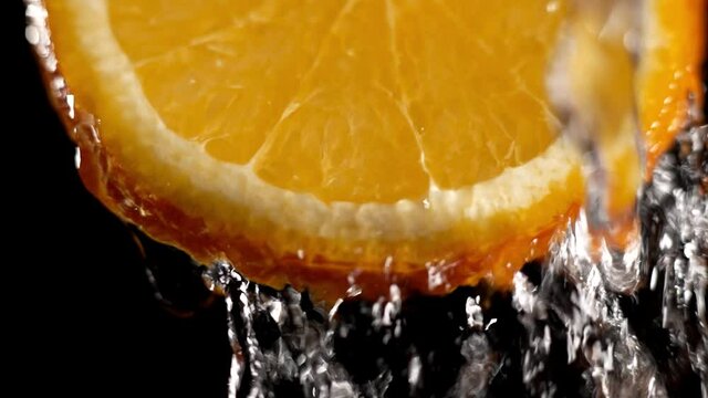 Water splashing on fresh orange in slow motion. Water dropping from citrus fruit. Close up orange slice rich in vitamin C.