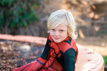 Little boy with long blonde hair sitting in golden sunlight wearing superhero costume