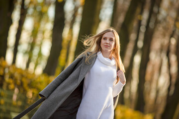 Pretty woman with light brown hair. Portrait of a beautiful woman in an elegant gray coat. Young woman walks in the autumn park.