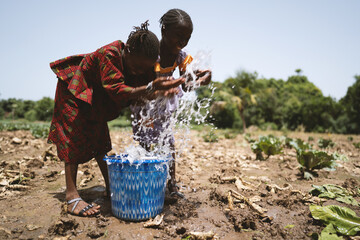 Two laughing thoughtless little African girls having fun wasting water regardless of the dry field...