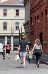 Rear view of a young couple walking down the street holding hands and shopping bags.