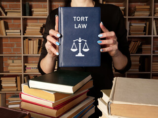 Lawyer holds TORT LAW book. A tort occurs when someone commits a wrong against another person - obrazy, fototapety, plakaty