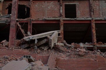 The wreckage of a new building. Demolition of the building. Piles of red brick fragments against the background of a metal skeleton.