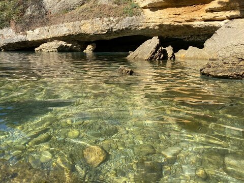 Sea pebble beach in paradise lagoon with cave grotto at summer. Smooth gravel and stones on seabed in transparent clear sea water. Beautiful seascape. Secluded place for relax and solitude. Awe rocks.