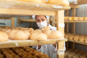Portrait of skilled Asian woman in white coat and protective face mask working in storehouse at...