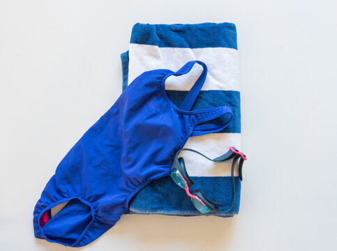 High angle view of blue and white swimming gear including towel, swimsuit and goggles on white background (selective focus)