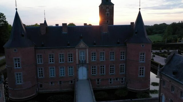Aerial circular shot of evening sunset view of Alden Biesen Castle in Belgium, Germany surrounded by square lake and greenery with cars passing by